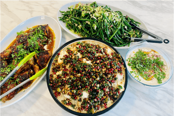 A Lendable in-house lunch, there are four plates including a dish containing pomegranate seeds, a platter of green beans, and grilled chicken