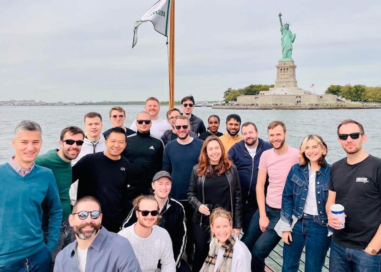 Team stood on a boat in front of the Statue of Liberty in New York